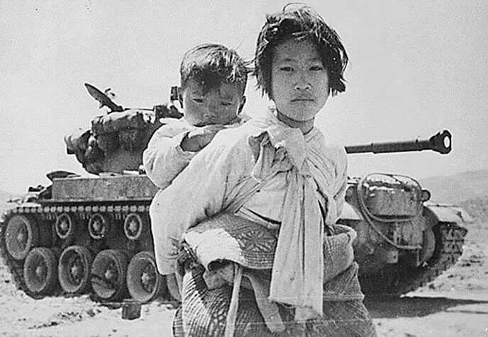 Little Girl Carrying Brother Walks by Tanks Fighting in Korean War