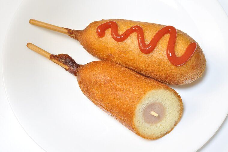 A vendor struggling with brittle and splitting hot dog buns decided to fry his meats in cornmeal batter, deliciously inventing the savory corn dog